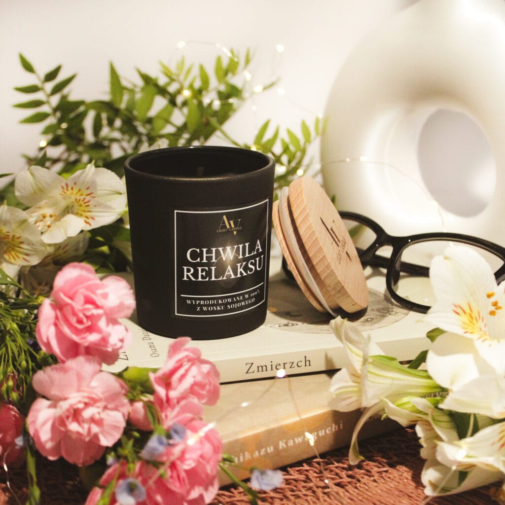 Czarna świeca sojowa Chwila Relaksu z kolekcji Ember otoczona kwiatami i książkami