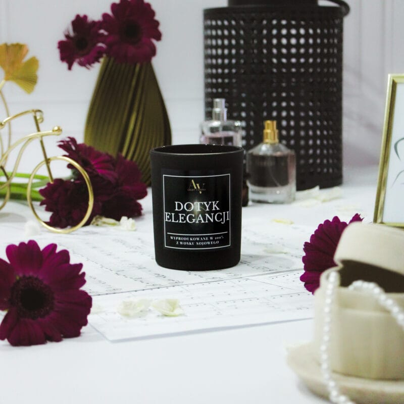 Zbliżenie na świecę Dotyk Elegancji w otoczeniu kwiatów i flakoników perfum