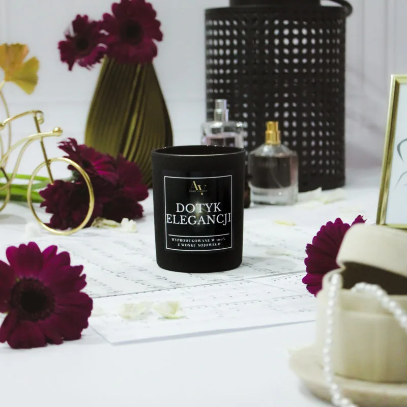 Zbliżenie na świecę Dotyk Elegancji w otoczeniu kwiatów i flakoników perfum