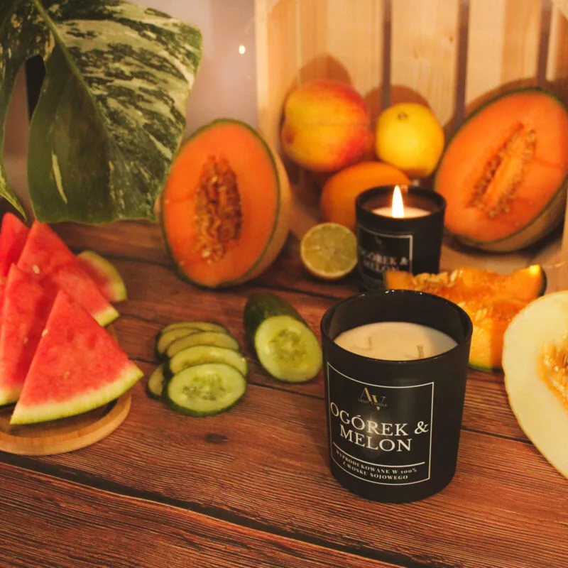 Świeca AV Light Candle w zapachu Ogórek i Melon, w matowym szkle, na tle świeżych ogórków i melona.
