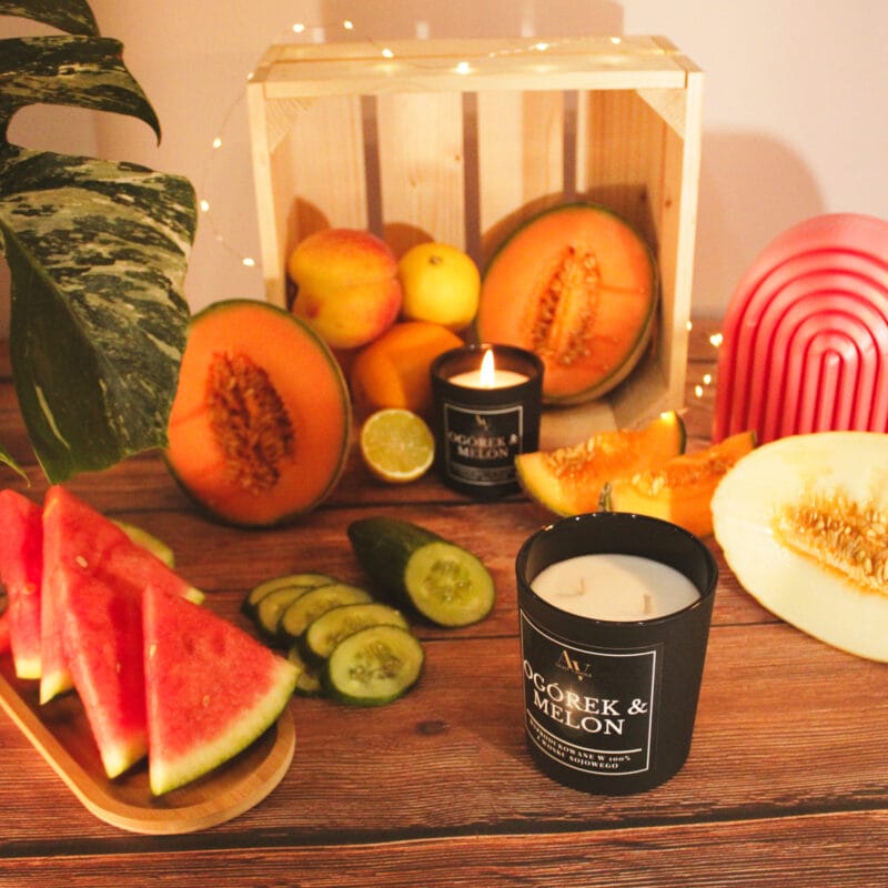 Świeca AV Light Candle w zapachu Ogórek i Melon, w matowym szkle, na tle świeżych ogórków i melona.