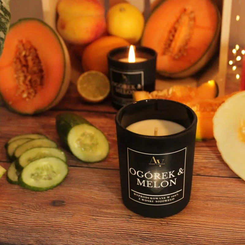 Świeca AV Light Candle w zapachu Ogórek i Melon, w matowym szkle, na tle świeżych ogórków i melona.