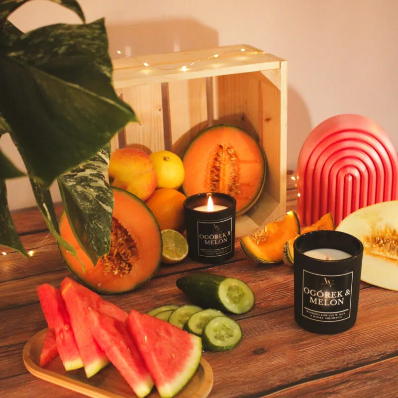 Świeca AV Light Candle w zapachu Ogórek i Melon, w matowym szkle, na tle świeżych ogórków i melona.