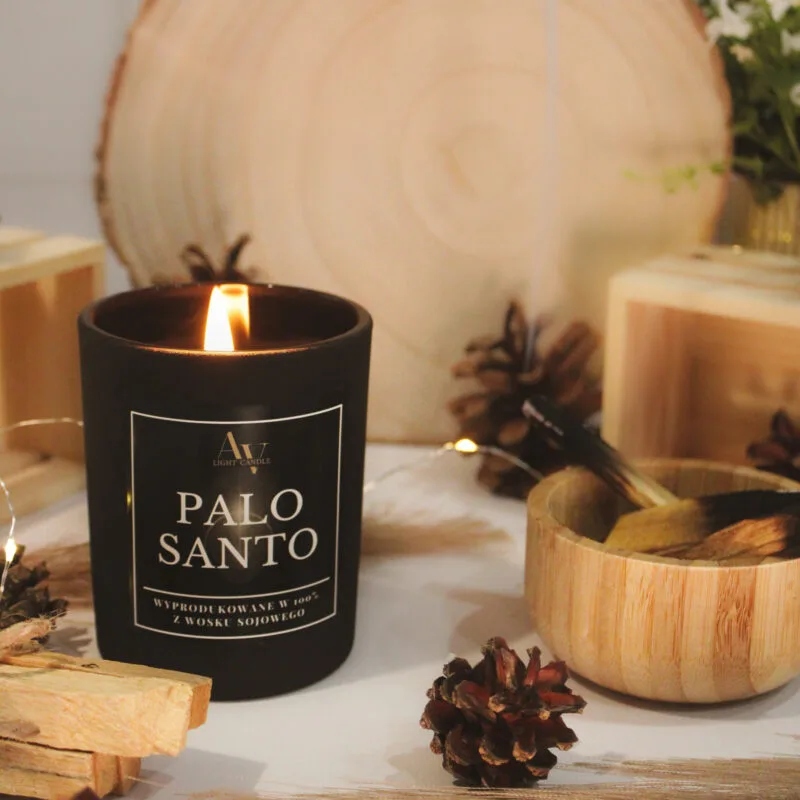 Świeca Palo Santo SENSE – zapalona wśród szyszek i drewna, aranżacja z boku