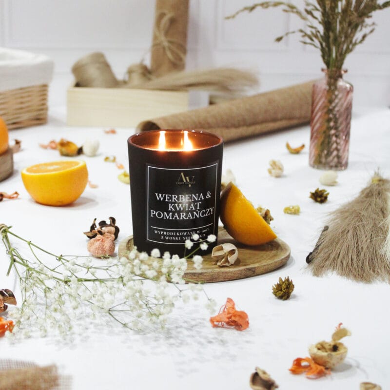 Zapalona świeca Werbena i Kwiat Pomarańczy AV Light Candle w czarnym szkle z kolekcji Lumor wśród naturalnych dekoracji.