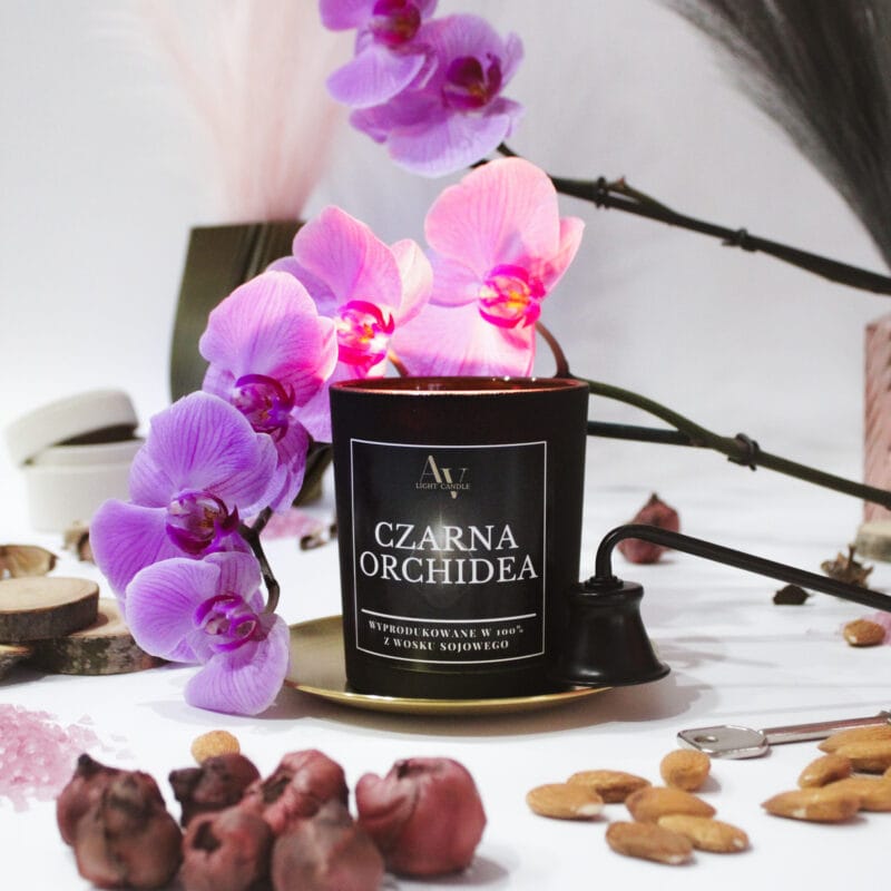 Świeca Czarna Orchidea Lumor otoczona płatkami orchidei i dodatkami zapachowymi na białym tle