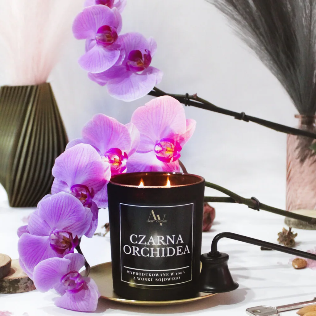 Czarna świeca sojowa AV Light Candle Czarna Orchidea z kolekcji Lumor w otoczeniu fioletowej orchidei
