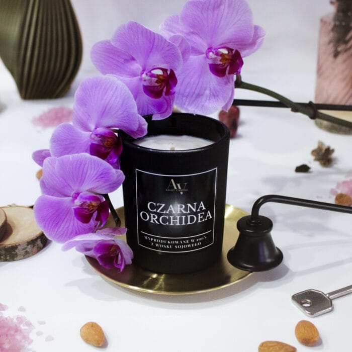 Świeca Czarna Orchidea AV Light Candle z serii Sense, w otoczeniu różowej orchidei i złotego talerza