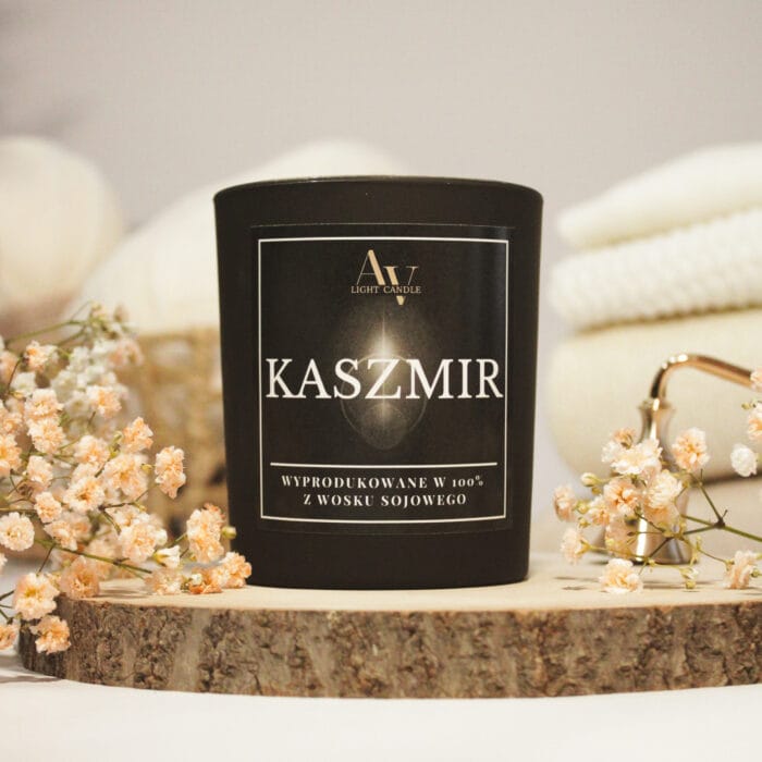 Zbliżenie etykiety świecy Kaszmir AV Light Candle – elegancki, czarny matowy słoik na tle kremowych pledów i gipsówki