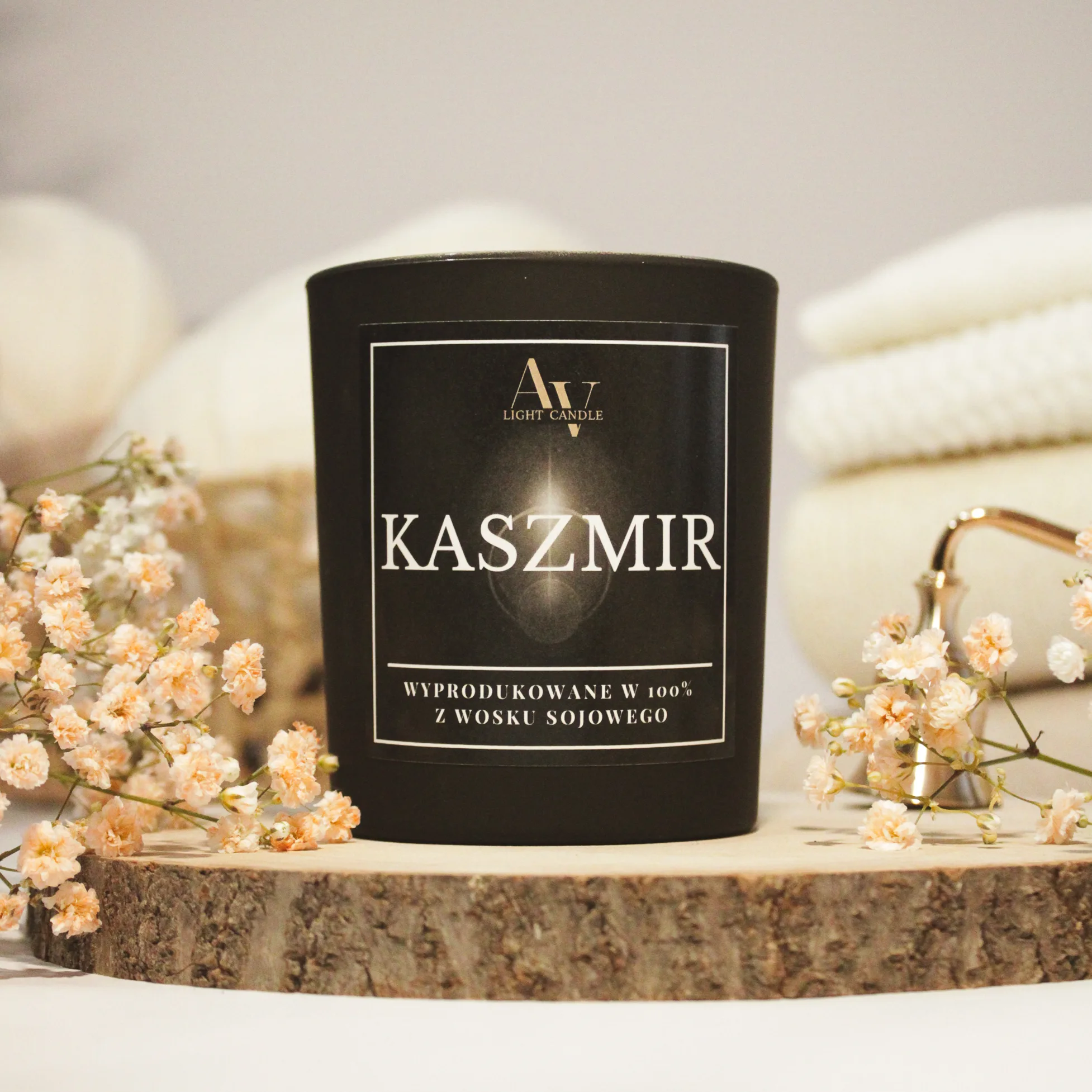 Zbliżenie etykiety świecy Kaszmir AV Light Candle – elegancki, czarny matowy słoik na tle kremowych pledów i gipsówki
