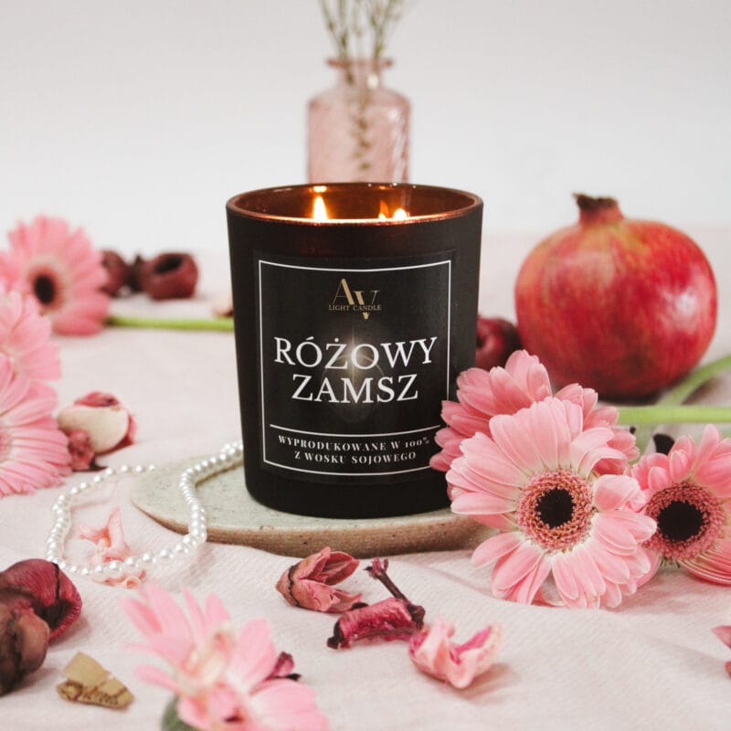 Świeca Różowy Zamsz Lumor AV Light Candle zapalona, otoczona różowymi kwiatami, granatem i perłami