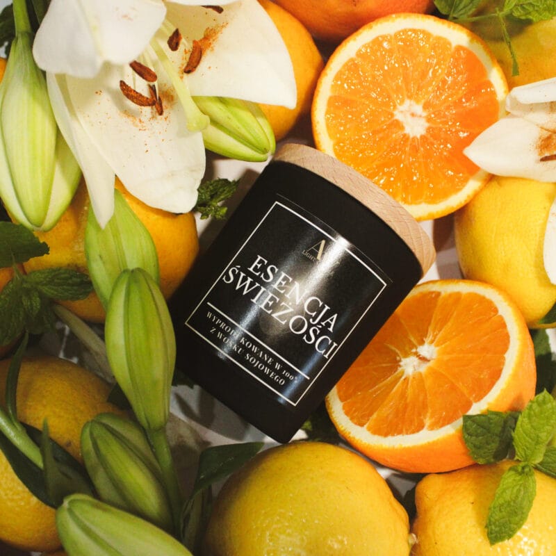 Świeca sojowa Esencja Świeżości AV Light Candle 130 ml z drewnianym wieczkiem w otoczeniu kwiatów i świeżych cytrusów.