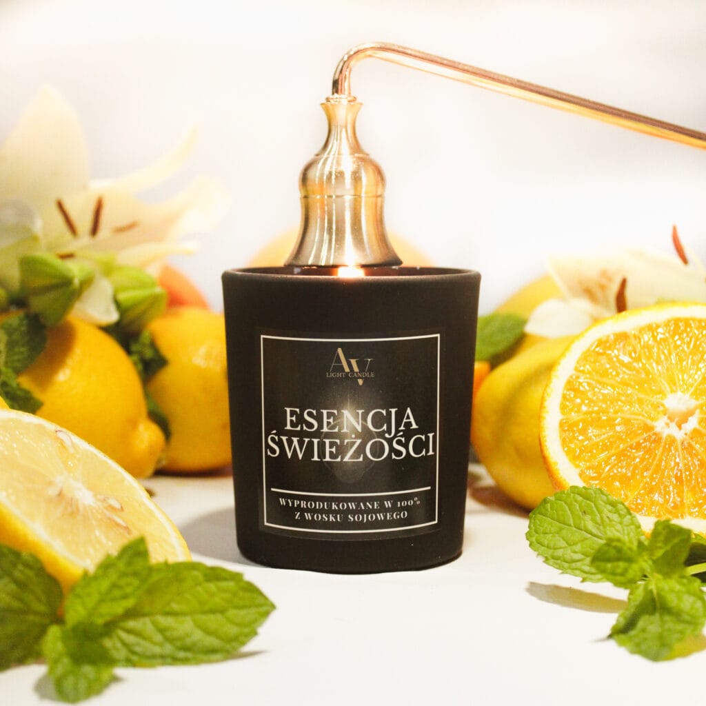 Świeca sojowa Esencja Świeżości AV Light Candle 130 ml w czarnym matowym szkle z gasidłem, w otoczeniu pomarańczy, cytryn i kwiatów.