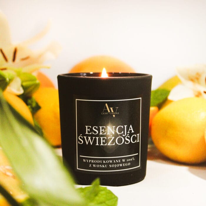 Płonąca świeca sojowa Esencja Świeżości AV Light Candle 130 ml w czarnym matowym szkle, w otoczeniu pomarańczy i lilii.