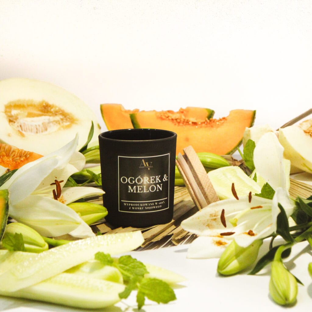 świeca sojowa ogórek i melon ember 130 ml w czarnym szkle w otoczeniu świeżych melonów, ogórków i kwiatów lilii