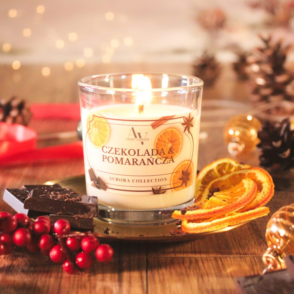 Zapalona świeca Czekolada i Pomarańcza z kolekcji Aurora – aranżacja z czekoladą i suszoną pomarańczą na tle świątecznym