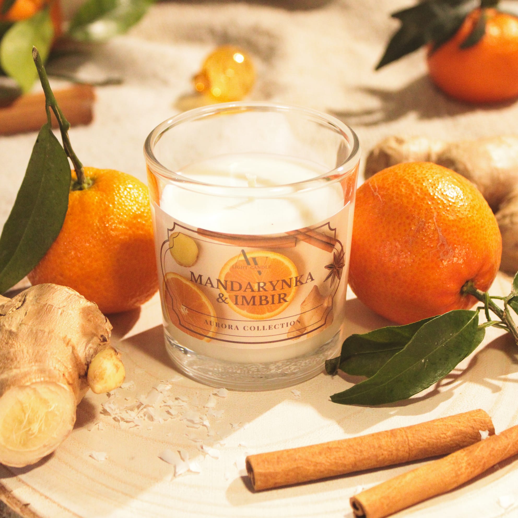 Świeca sojowa Mandarynka & Imbir – zapalona, zbliżenie na etykietę i jasne cytrusowe tło