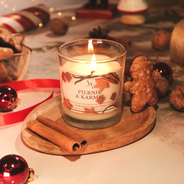Świeca sojowa Piernik i Karmel 130 ml z kolekcji Aurora – zapalona, ustawiona na drewnianej podstawce w świątecznej aranżacji z cynamonem, pierniczkiem i bombkami