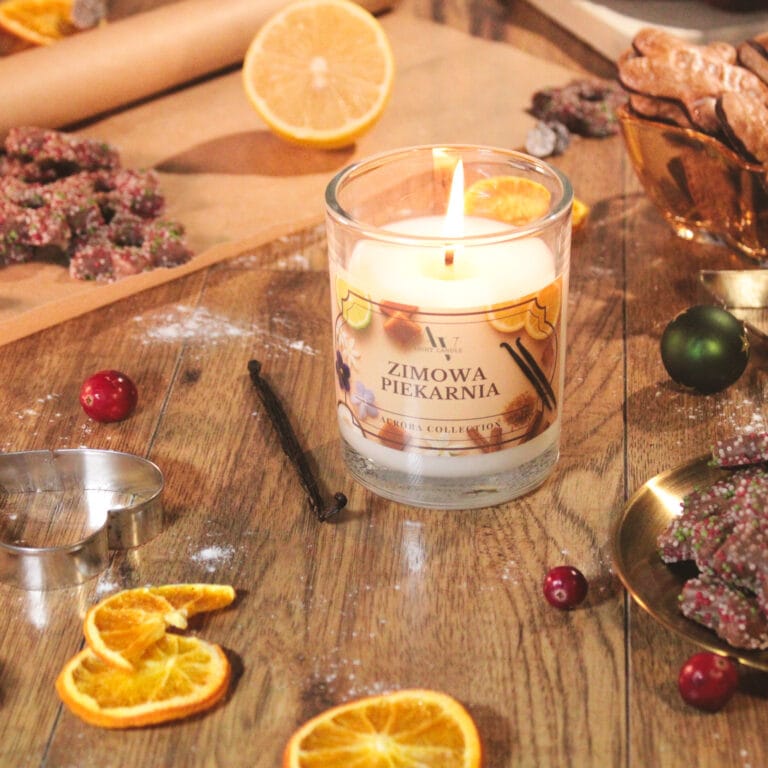 Świeca Zimowa Piekarnia AV Light Candle 200 ml – edycja Aurora, zapalona, otoczona suszonymi plasterkami pomarańczy, przyprawami i świątecznymi dekoracjami
