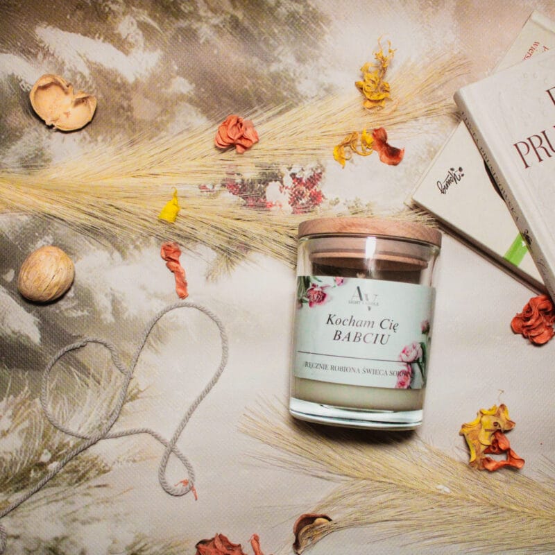 Ręcznie robiona świeca sojowa „Kocham Cię Babciu” w transparentnym szkle z drewnianą pokrywką, ujęcie na jasnym, dekoracyjnym tle